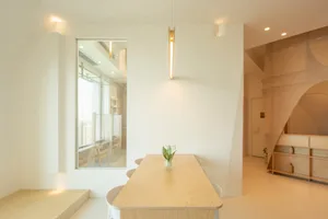 Minimalist living room with a wooden table and chairs, white walls, and a large window.