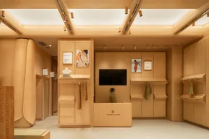 A modern retail shop with a wooden interior, featuring a central display area, shelves, and a television screen.
