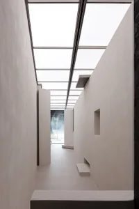 A minimalist corridor with concrete walls and floors, illuminated by a ceiling skylight.