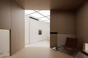Modern minimalist residential interior with wooden walls and floor, a chair, and a view of the kitchen area.