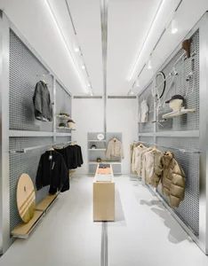 Modern retail store interior featuring metal grid panels, wooden display furniture, and glass shelves.