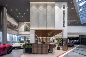 Modern minimalist car dealership reception area with metal accents, wood finishes, and glass partitions.