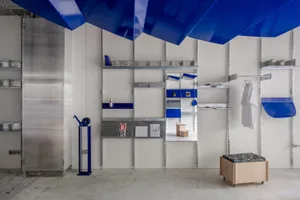A minimalist workspace featuring metal shelving units and a blue canopy.