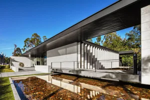 Modern exterior building made of concrete with a large overhanging roof and a reflecting pool with rocks.
