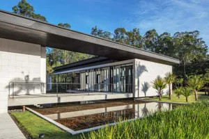 Modern residential exterior with concrete walls and a swimming pool surrounded by greenery.