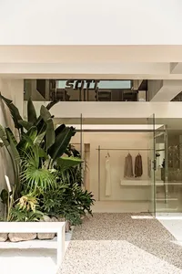 Modern minimalist clothing retail store featuring glass and concrete materials on a tiled floor.