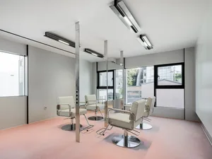 Modern minimalist salon featuring a white metal pole and white chairs against a pink floor.