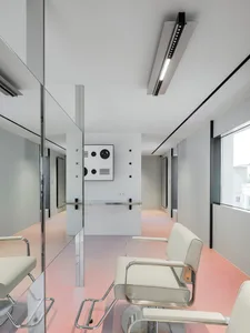 A minimalist white interior of a hair studio, featuring sleek modern chairs, a counter with a mirror, and large windows allow