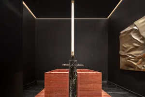 Modern bathroom with a sleek, elegant marble sink and a tall, vertical light fixture in a dark, minimalist space.
