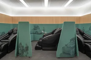 A modern interior seating area with black massage chairs and green dividers.