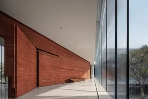 A modern interior corridor featuring wooden walls and floor with large windows allowing natural light to fill the space.