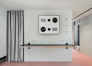 A minimalist interior design featuring a concrete wall and a black shelf with a speaker system.