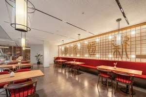 A modern restaurant interior featuring red upholstered seating and wooden tables.