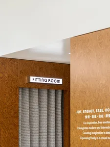 Close-up of a fitting room with a wood-textured wall and a gray curtain in a fashion retail store.