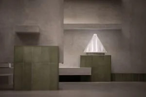 A minimalist interior space with concrete walls and floors, featuring green tiles and a white triangle light fixture.