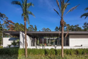 Modern residential exterior featuring concrete walls and large glass windows against a clear blue sky.