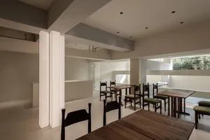 A modern minimalist restaurant interior featuring wooden tables and chairs.