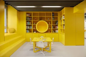 A vibrant yellow playroom with a circular cut-out, a yellow table and chairs, and various books and toys.