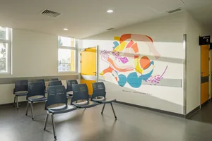 A modern waiting room with colorful abstract mural, blue chairs, and yellow doors.