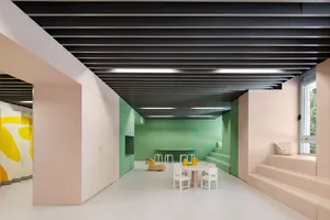 A modern playroom with green walls, white furniture, and colorful toys on the floor. The room features a small table and chai