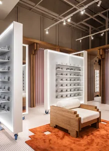 A modern retail display featuring a white panel with glass shelves and wooden armchair on a terracotta rug.