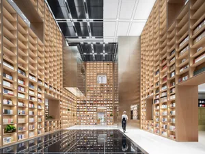 Library interior with minimalist design featuring wooden shelves and glass elements.