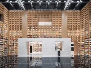 Modern library interior with tall bookshelves lined with books, a white floor, and a black ceiling with lights.