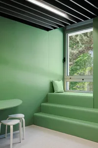 A minimalist green interior with a window seat and stools.
