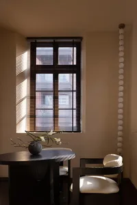 A minimalist interior designed with wooden elements, featuring a round table, chairs, and a vase with flowers under a window 