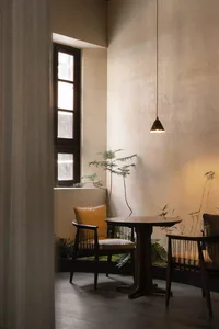 A cozy restaurant interior featuring a wooden table with a yellow cushion, green plants, and a hanging pendant light.