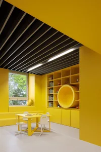 A modern, yellow-themed children's playroom with a seating area, table, and bookshelves.