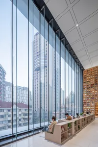 People sitting in a modern library with large glass walls overlooking the city.