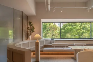 A modern, minimalist interior with white walls and wooden accents, featuring a large window overlooking greenery.