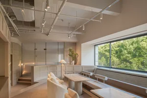Modern restaurant interior with white seating, tall table, and large window overlooking greenery.