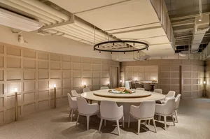 A modern restaurant with a circular table surrounded by white chairs, featuring wooden paneling walls and a circular light fi
