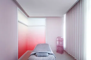 A minimalist bedroom with a gray blanket on a bed, pink gradient walls, and a pink plastic shelf unit.