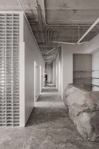 A modern corridor made of concrete with glass block walls and exposed ceiling pipes.