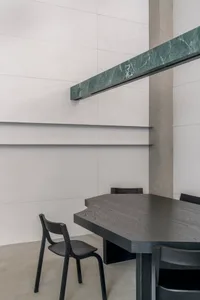A modern dining room featuring a blackwood table and chairs, white walls, and a green marble shelf.