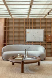 A modern living room featuring a curved sofa, a round coffee table, and a whiteboard on a wooden grid wall.
