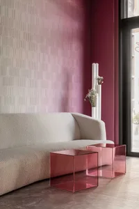 A minimalist living room featuring a textured wall, a beige sofa, and two pink acrylic cube tables.
