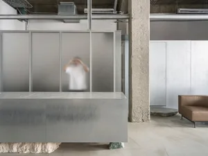 A modern office space featuring concrete walls, glass partitions, and metallic elements.