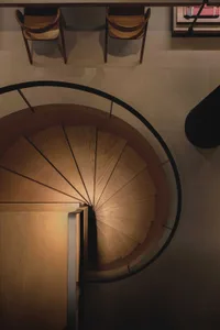 A modern wooden staircase with black railings viewed from above, showing the spiral design and landing.