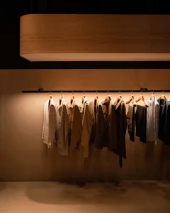 A row of clothing hangers displaying various garments, illuminated by warm lighting.