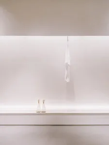 White minimalist boots on a concrete ledge with a hanging towel, all under a white surface with hidden lighting.