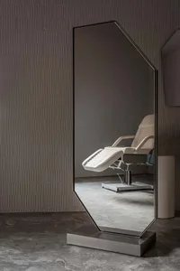 A minimalist floor mirror with a metal frame sits against a textured wall in a modern interior space.