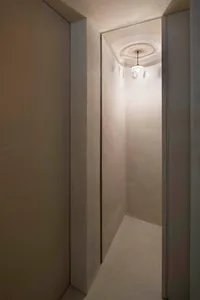 A minimalist bathroom with a concrete floor and walls, illuminated by a single chandelier.
