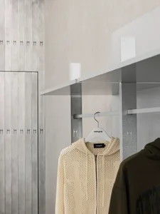 A minimalist clothing retail space with metallic shelves and a beige knit sweater hanging on a hanger.