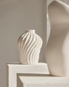 A minimalist, abstract white ceramic vase with wavy lines sits on a white pedestal in a neutral, minimalist setting.