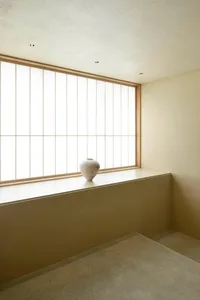 A minimalist indoor space featuring a white ceramic urn on a ledge with a large window.
