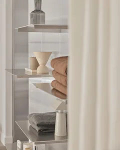A modern bathroom with metal shelves containing neatly folded towels, decorative items, and toiletries.